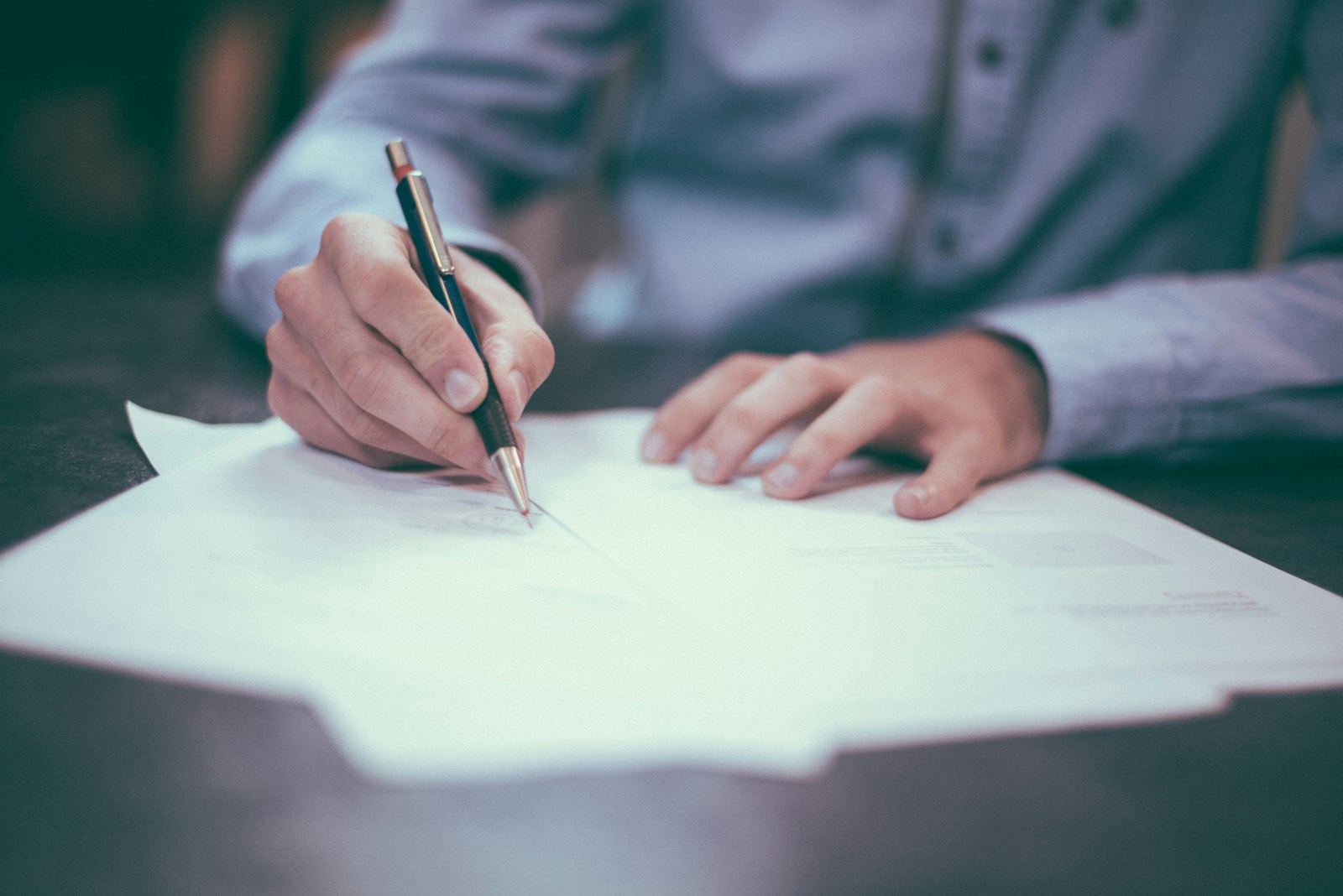A person signing a document at a desk with a pen